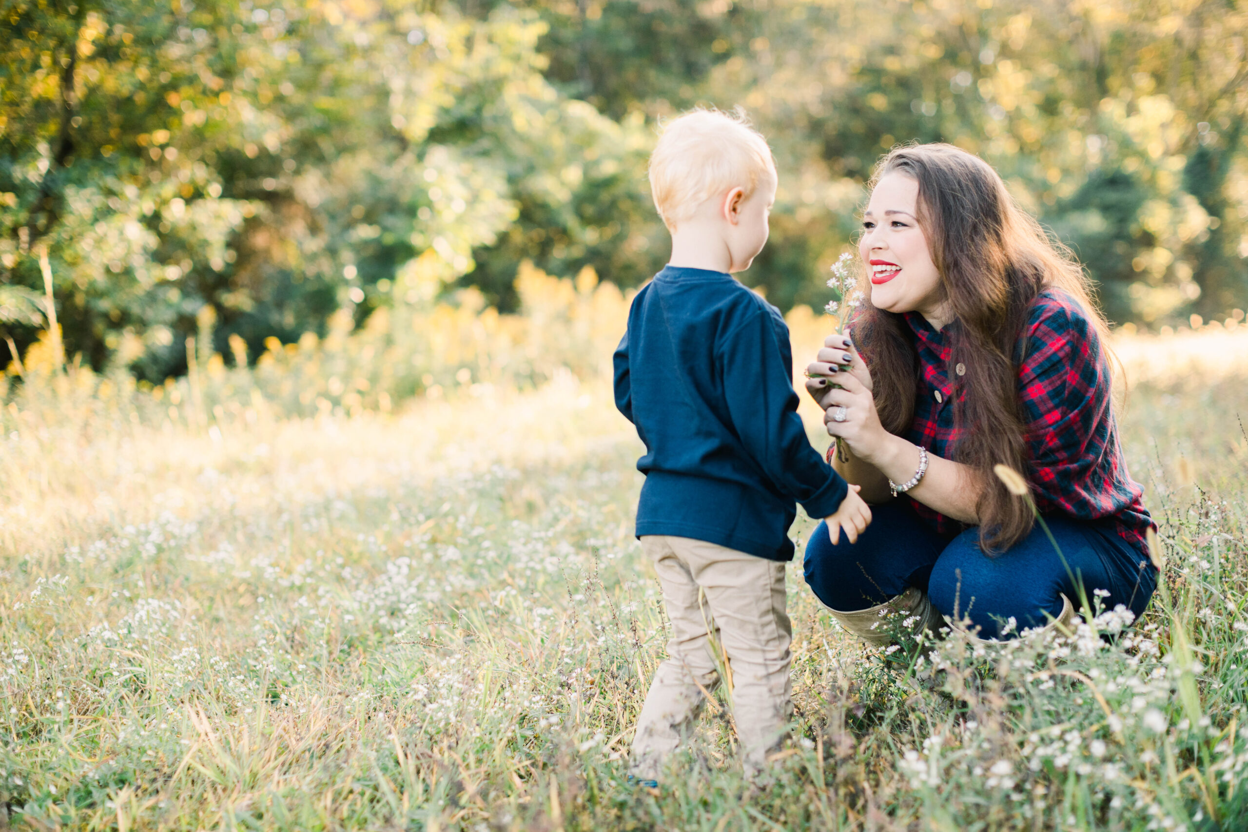 mom kneeled down with toddler in a field handing boy a flower