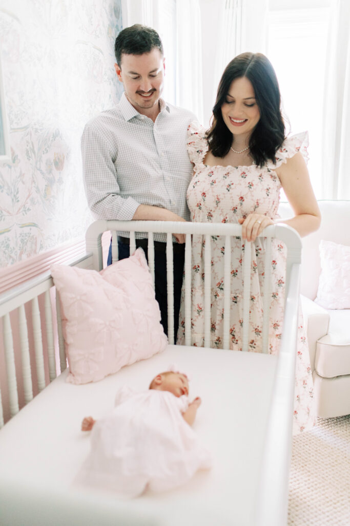 mom and dad looking over crib at their newborn baby girl in her nursery 