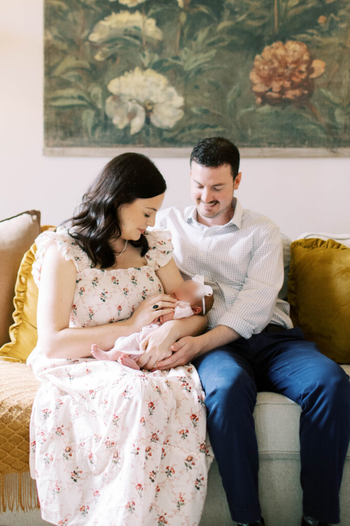 mom and dad in living room holding newborn girl on their couch 