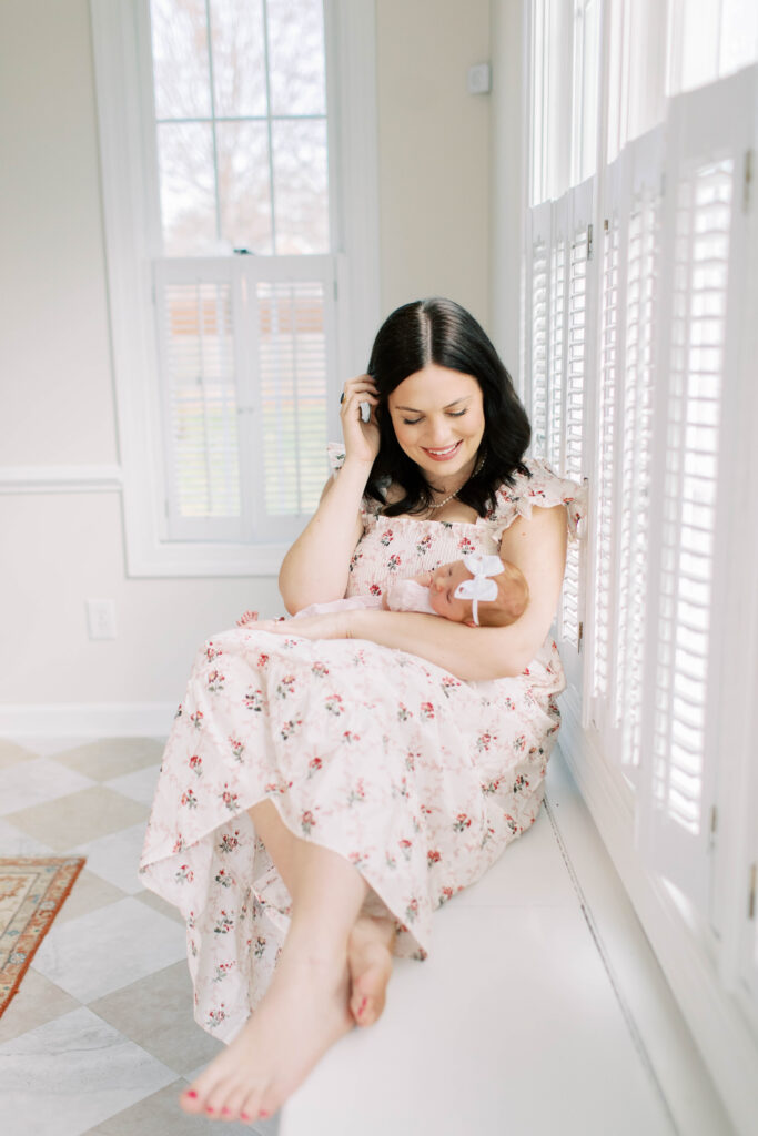 mom holding newborn baby girl in kitchen sitting on the ledge in front of windows