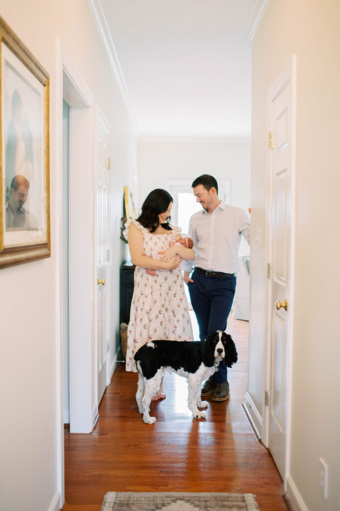 mom and dad holding baby girl in hallway with their dog