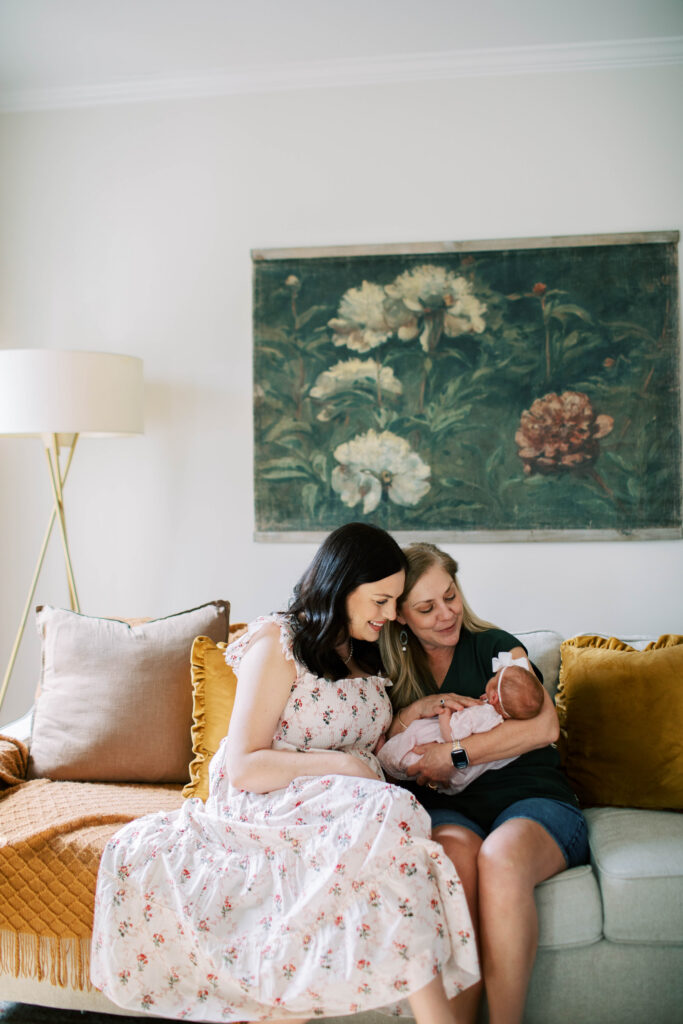 mom and grandma holding and looking at baby girl on living room couch 