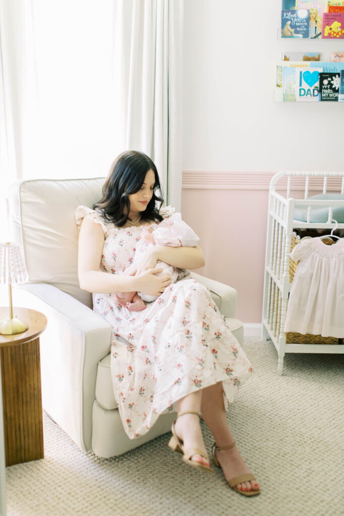 mom in floral flowy hill house dress holding newborn baby girl in recliner 