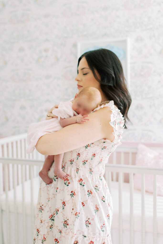 mom in floral flowy hill house dress holding newborn baby girl up on her shoulder 