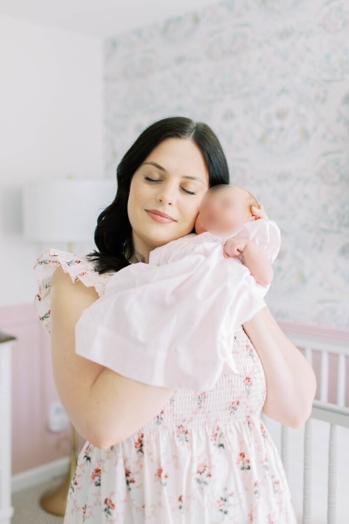 mom in floral flowy hill house dress holding newborn baby girl yo to her face