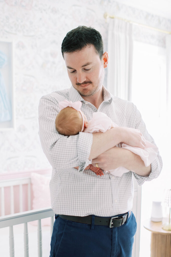 Dad holding newborn baby girl in nursery 