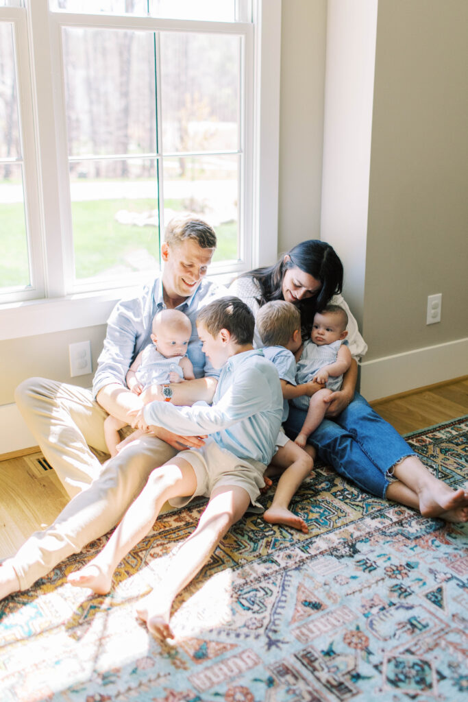family snuggled up together with their 4 boy kids by window 