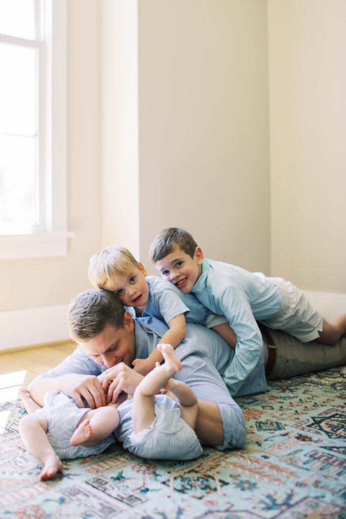 dad laying on ground with 4 boy kids while 2 ride his back 