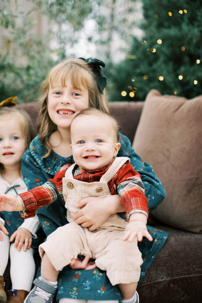 baby brother sitting on big sisters lap with a christmas tree in the background
